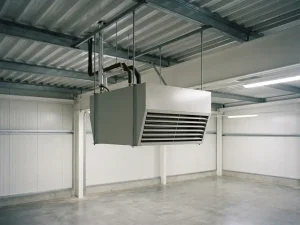 Lichtgrijze luchtverwarmer opgehangen aan stalen gordingen onder een golfplaten dak, met gelamelleerd uitblaasrooster en leidingaansluitingen bovenop.